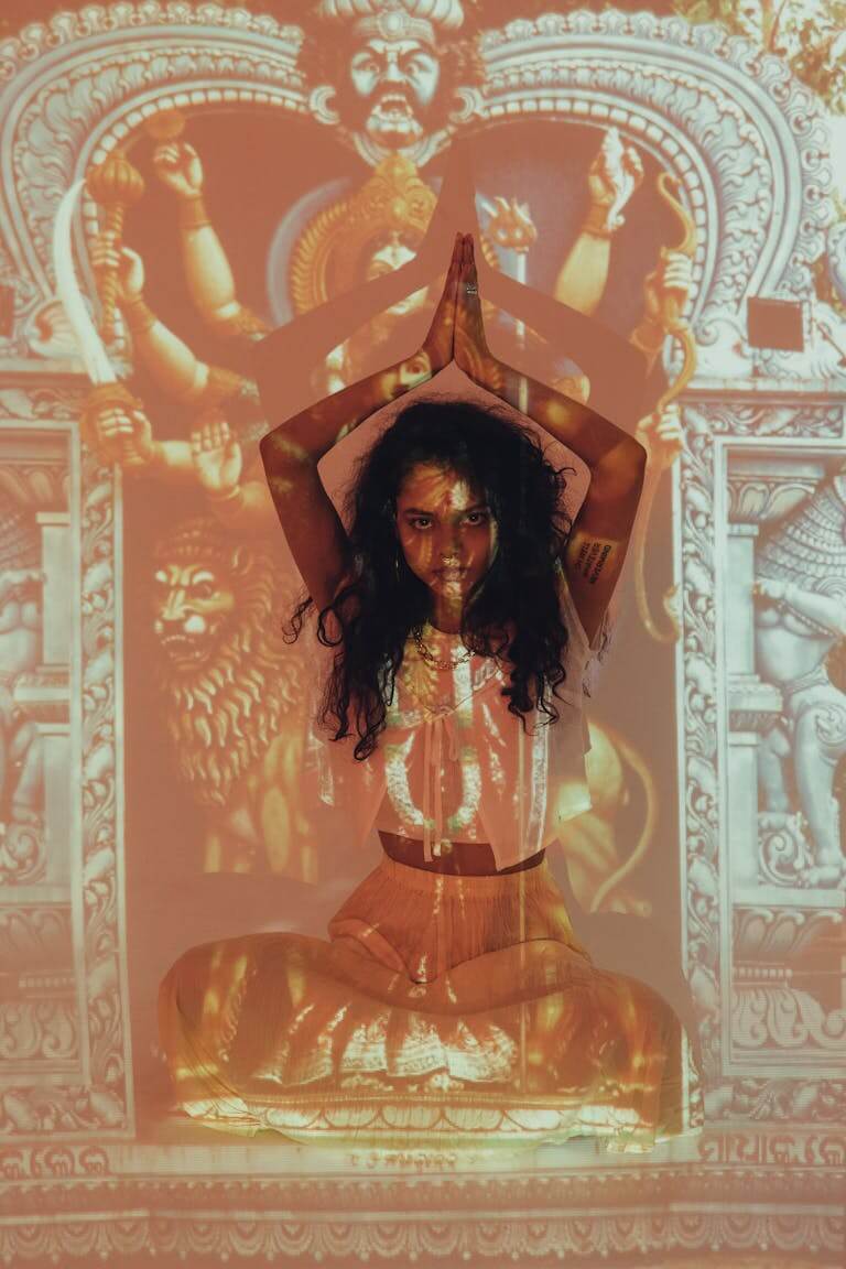 A woman in a meditative pose with Indian cultural projections in a studio setting.