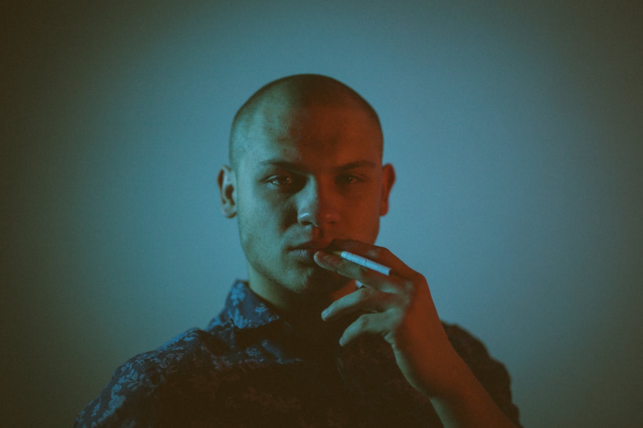 Moody portrait of a bald man smoking against a blue background, capturing introspective mood.