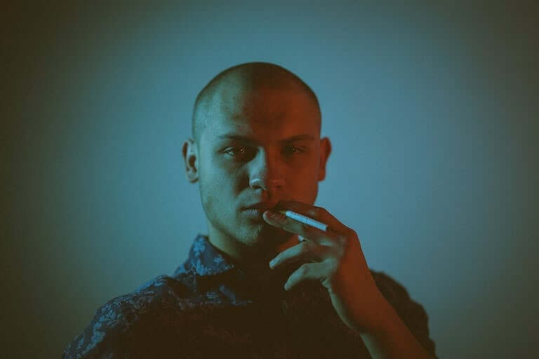 Moody portrait of a bald man smoking against a blue background, capturing introspective mood.