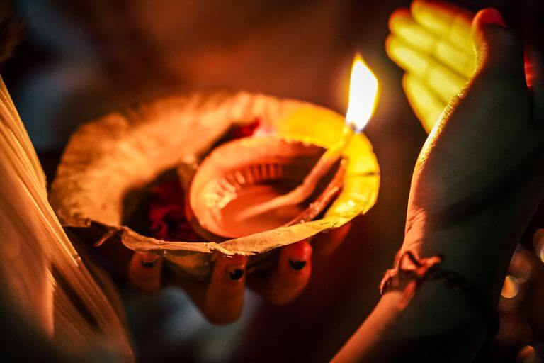 Close-up of a hand holding a diya lamp during a cultural festival, showcasing warm light.